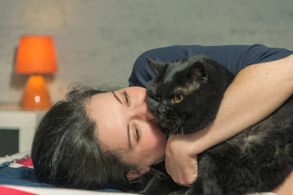 Kot. Dziewczyna leży na łóżku w uścisku z czarnym kotem — Zdjęcie stockowe