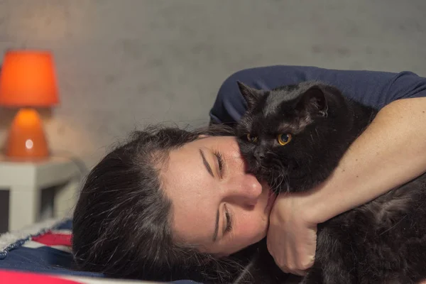 ¡Cat! Una chica yace en una cama en un abrazo con un gato negro —  Fotos de Stock