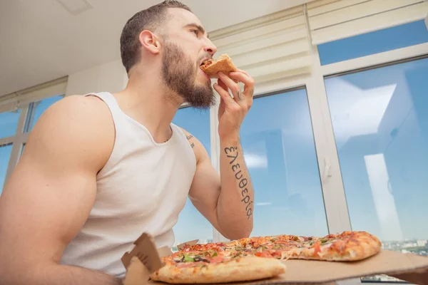 Pizza. A guy with a beard eats pizza