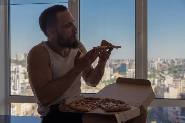 Pizza. A guy with a beard eats pizza