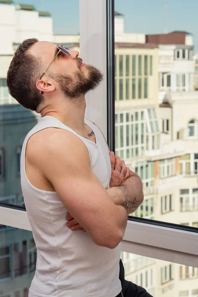 A guy with a beard looks out the window — Stock Photo, Image