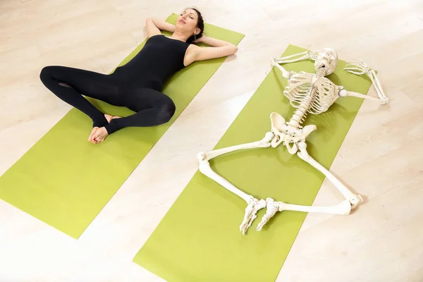 A menina está envolvida em ioga, juntamente com o esqueleto — Fotografia de Stock