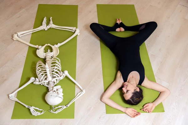 The girl is engaged in yoga along with the skeleton — Stock Photo, Image