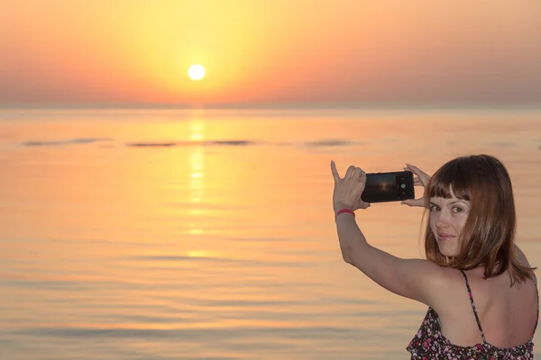 女の子は携帯電話で夕日を取っています。 — ストック写真