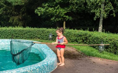 Küçük kız havuzu yapraklardan temizliyor.