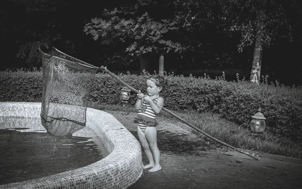 Klein meisje reinigt het zwembad van de bladeren — Stockfoto