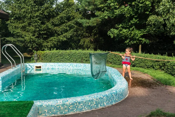 Little girl cleans the pool from the leaves