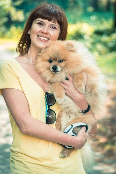 A girl is walking with a park with a dog. Pomeranian Spitz — Stock Photo, Image