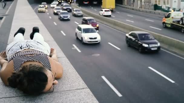 Highway. Flickan liggande på trottoaren nära motorvägen — Stockvideo