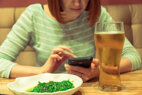 Mobiltelefon. En tjej i en bar ser ut på skärmen på en mobil ph — Stockfoto