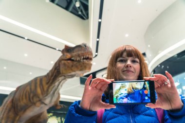 Kız selfie bir dinozor arka plan üzerinde yapar.