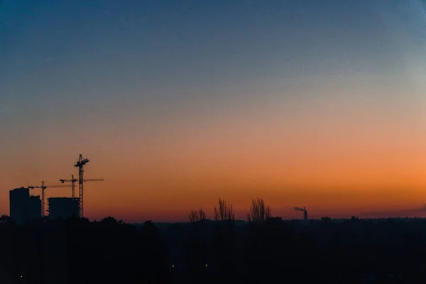 Morgengrauen. Silhouetten von Häusern und Baukränen — Stockfoto