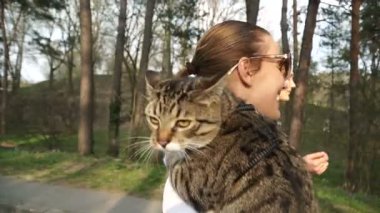 Kedi bir leash üzerinde. Bir kız omuzunda oturur bir kedi ile yürüyor