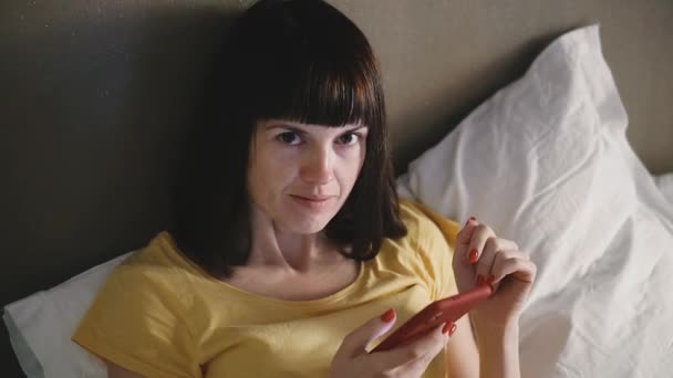 携帯電話だ女の子はベッドに横になって携帯電話を見て — ストック動画