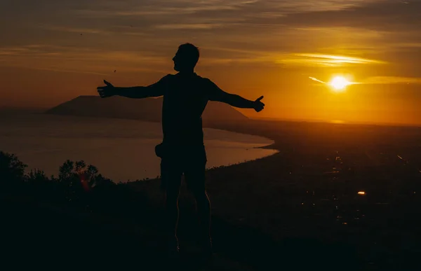 旅だ男が山の上に立って夕日を見る — ストック写真