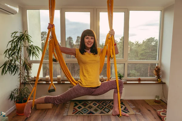 Fly Yoga. Woman doing yoga exercises on a hammock in an apartment.