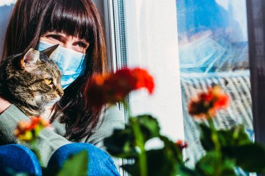 Virüs. Bir kadın, virüsten korunan gazlı bez maskeli bir kediyle oturuyor..