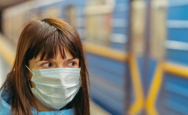 Tıbbi maske. Tıbbi maskeli bir kadın metroda tren bekliyor. Ukrayna. Kiev.