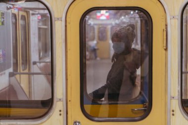 Tıbbi maske. Tıbbi maskeli bir kadın metro trenine biniyor. Ukrayna. Kiev.