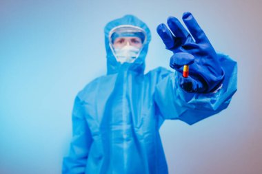 Virüs. Virüse karşı koruyucu giysi giyen bir sağlık görevlisi elinde bir hap tutuyor..