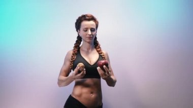 Diyet olsun. Spor kızı elinde bir elma ve bir pasta tutuyor..