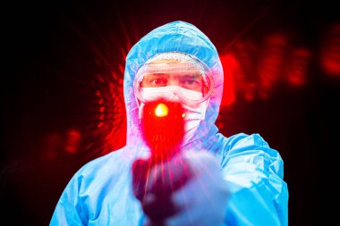 Temassız termometre. Koruyucu antivirüs giysisi giymiş bir adam elinde bir termometre tutuyor..