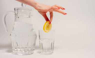 İçme suyu. Bir kadın eli bir bardak suya limon atar..