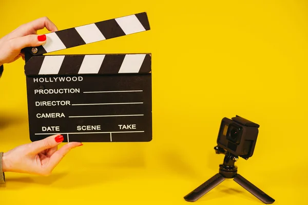 Movie clapper board. A hand holds a movie clapperboard next to a small video camera.