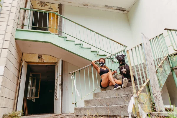 Post apocalypse. Athletic girl in a hypoxic mask holds a dog on a leash.