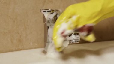 Temizlik. Koruyucu eldivendeki bir el banyodaki musluğu bir bez ve deterjanla yıkar..