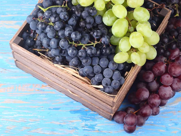 Verse druiven van verschillende kwaliteiten in een houten doos op een blauwe houten achtergrond met ruimte voor de tekst. Bovenaanzicht. Rechtenvrije Stockfoto's