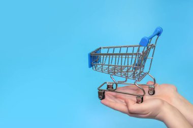 Mavi arka planda izole edilmiş kadın ellerinde alışveriş arabası. Çevrimiçi alışveriş kavramı..
