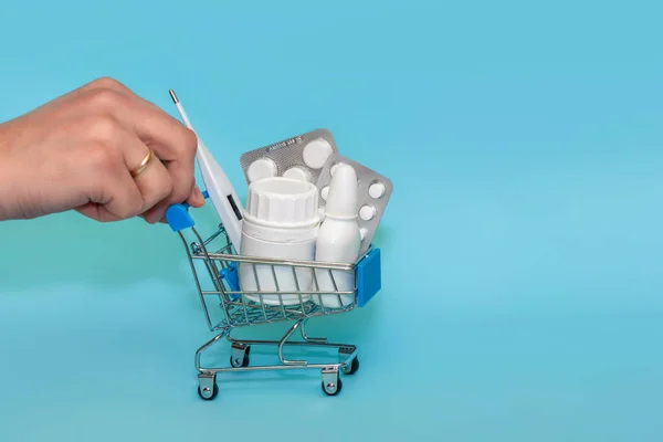 青い背景に丸薬でいっぱいのショッピングカートで男性の手のクローズアップ オンラインショッピングの薬の概念 テキストのコピースペース — ストック写真