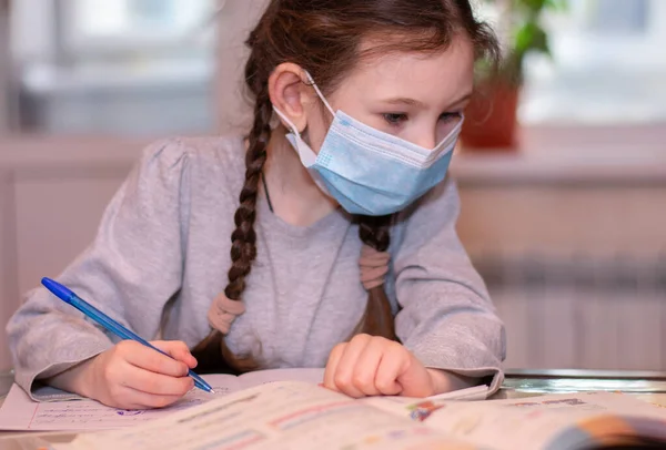 Uzaktan eğitim. Tıp maskeli kız evde ödev yapıyor. Karantina.