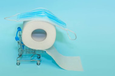 Bir alışveriş arabasında tuvalet kağıdı rulosu ve tüketici paniğinin sembolü olarak tekerlekli el arabasında tıbbi maskeler. Coronavirus.