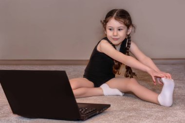 Güzel küçük kız evde spor egzersizleri yapıyor, dizüstü bilgisayar ekranına bakıyor. Kişisel antrenörle uzak eğitim. Evde kal, sosyal mesafeyi koru, Coronavirus karantinası sırasında kendini izole et.