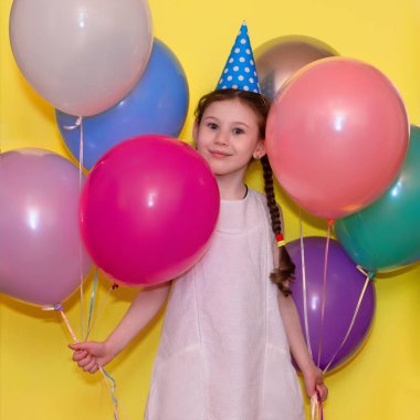 Doğum günün kutlu olsun! Sarı arka planda balonları ve şapkası olan mutlu kız.