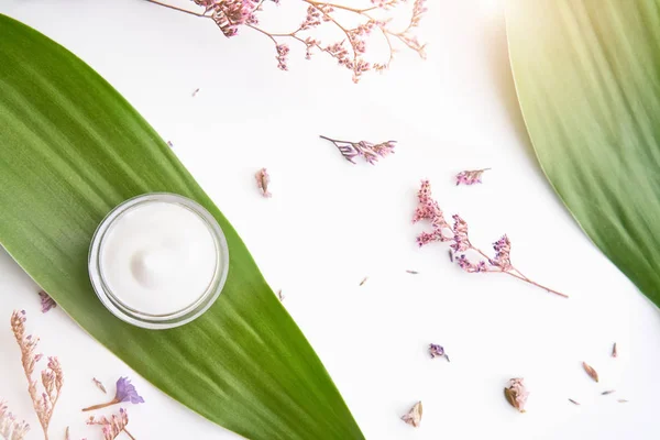 Beyaz krem şişesi yerleştirilir, sahte için boş etiket paketi kadar bir yeşil yeşillik arka plan ve çiçekler. Doğal güzellik ürünleri kavramı.