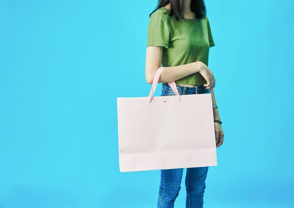 女人穿着绿色衬衫里的蓝色背景拿着购物袋. — 图库照片