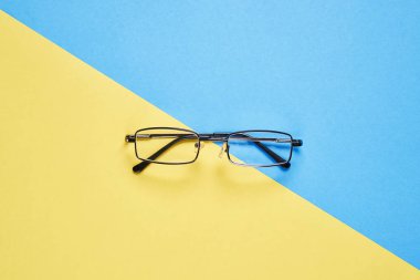 Pastel sarı ve mavi zemin üzerine yerleştirilmiş gözlük yarım böler.