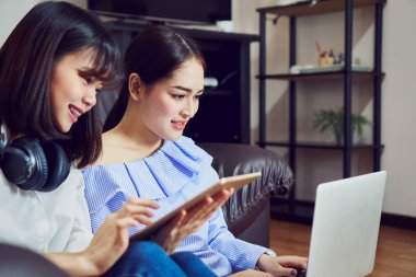 Asyalı kız mavi casual elbise siyah kulaklık ve kullanım laptop müzik. Bir rahat ve iyi ruh hali içinde kanepe oturma odasında.