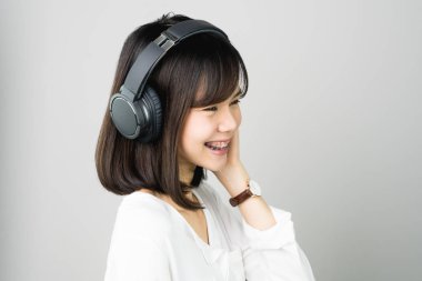 Asyalı kız beyaz casual elbise siyah kulaklık müzik. Rahat ve iyi bir ruh halinde gri bir arka plan üzerinde yumuşak bir ışık verir..