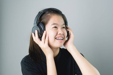 Asyalı kız siyah casual elbise siyah kulaklık müzik. Rahat ve iyi bir ruh halinde gri bir arka plan üzerinde yumuşak bir ışık verir..