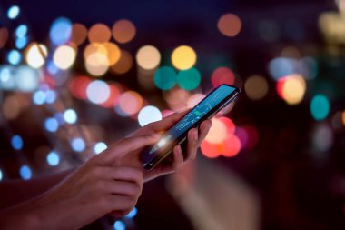 Gece atmosferik şehirde cep telefonunun kilidini açmak için akıllı telefondaki parmak izlerini tarayan eller, kimlik teknolojisindeki güvenliği kavrıyor..