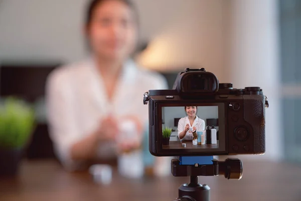 Genç Asyalı kadın güzellik vlogger videosu çevrimiçi kozmetik ürünlerinde ve dijital kamerada canlı videoda gösteriliyor.