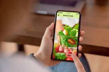Evdeki masada salata siparişi vermek için akıllı telefon kullanan ve uygulama ekranına dokunan kadın.