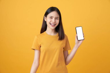 Neşeli, güzel Asyalı kadın açık sarı arka planda akıllı telefonu tutuyor..