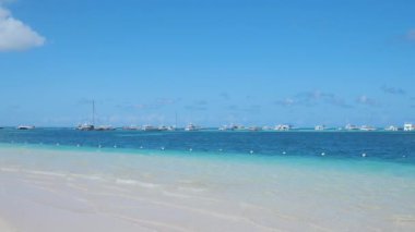 Atlantik Okyanusu 'nun turkuvaz rengi su ve açık mavi gökyüzü üzerinde beyaz kumlar üzerinde dalgalar. Yatlar ve tekneler ufukta demirlemişti. Karayipler, Punta Cana Dominik Cumhuriyeti