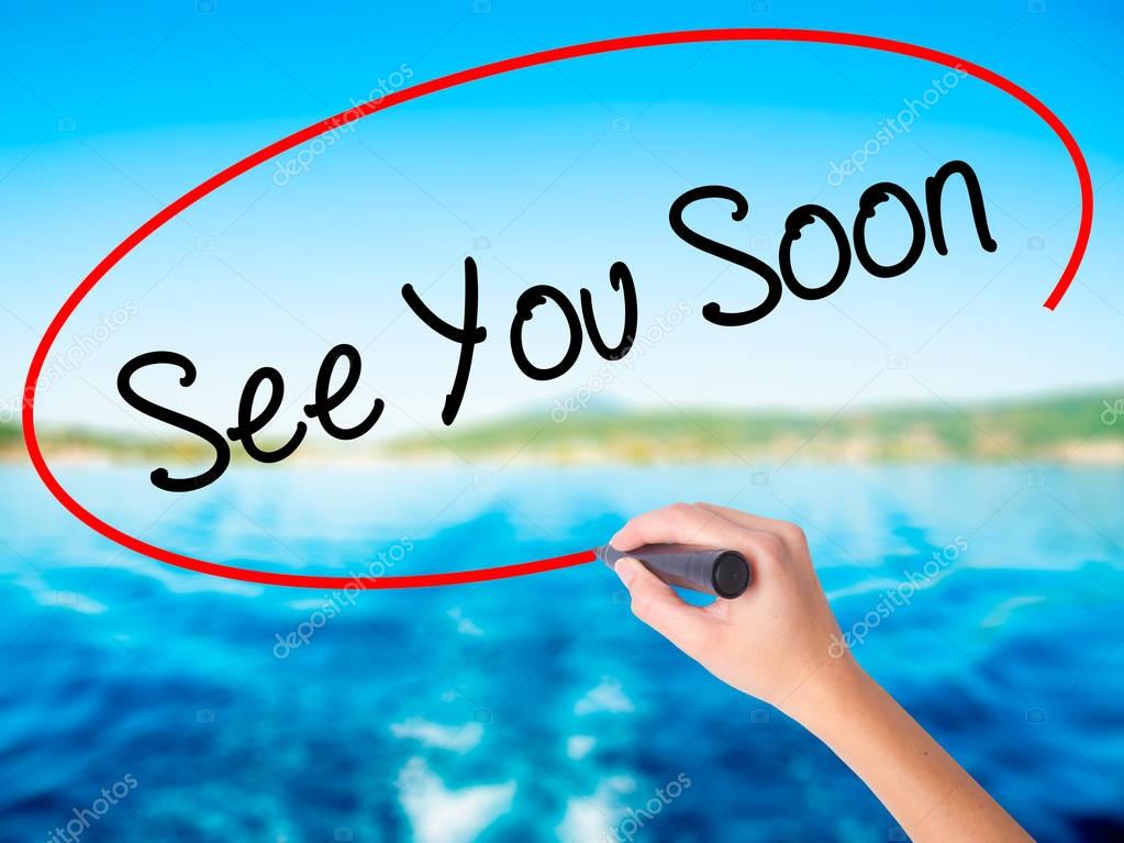 Woman Hand Writing See You Soon on blank transparent board with a marker isolated over water background. Business concept. Stock Photo