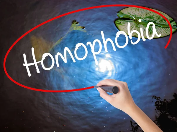 Frau schreibt Homophobie mit Filzstift über transparente Tafel — Stockfoto